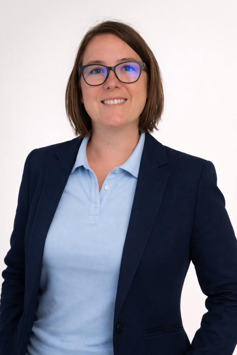 Foto der Prokuristin Foto er Prokuristin, sie trägt einen dunkelblauen Blazer und ein hellblaues Polohemd darunter, sie lächelt freundlich in die Kamera